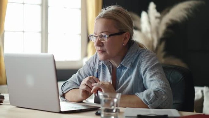 老年女商人在互联网上读坏消息，摘下眼镜，关上笔记本电脑。工作中的坏消息