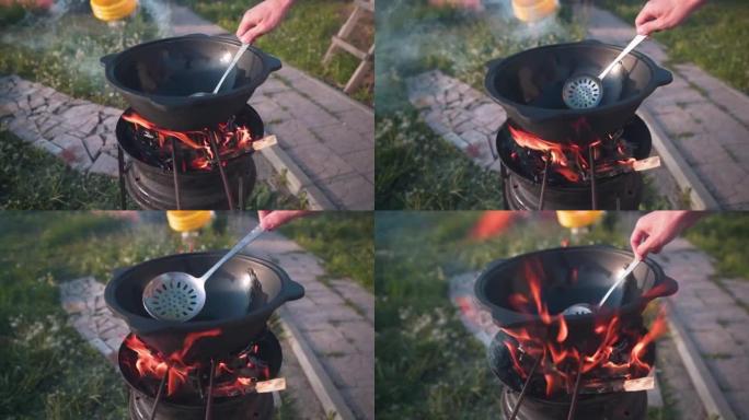 在明火上做饭的大锅，在火上做饭。男人的手搅动了油