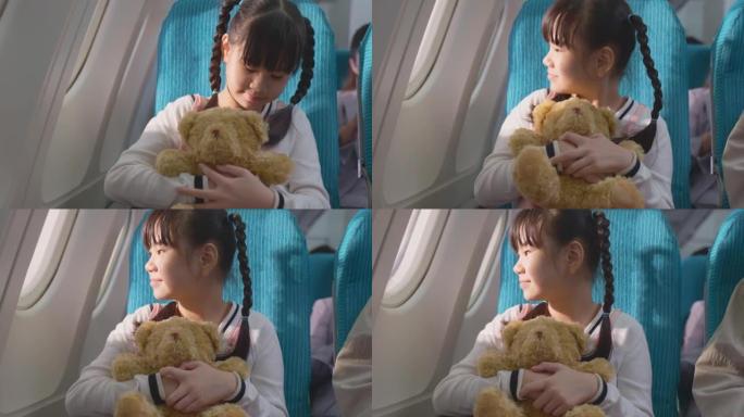 亚洲年轻小女孩拥抱熊娃娃，坐在飞机上的肖像。这个孩子和家人一起旅行感到兴奋和快乐。乘客在飞机上的运输
