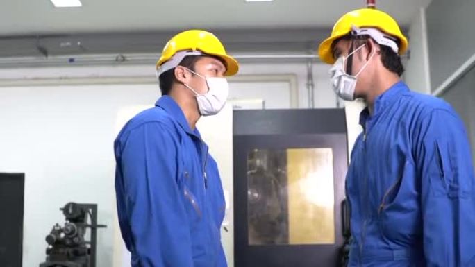 穿着安全制服的亚洲男性工人戴着防护口罩与同事击掌并谈论工厂工业建设的工作