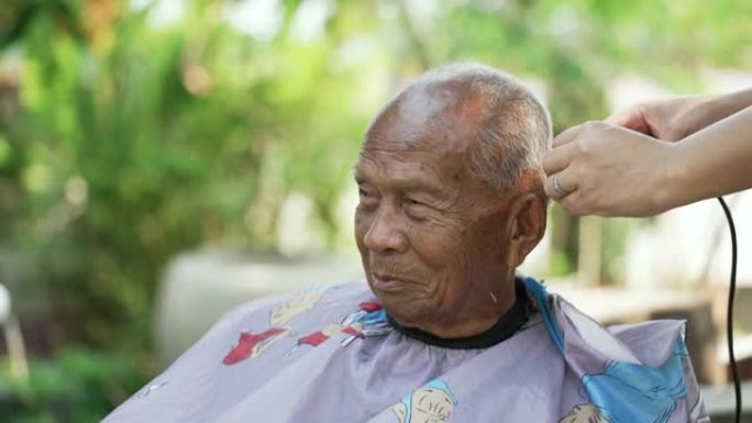 在检疫冠状病毒期间，亚洲妇女正在自家后院剪发和修剪老人的头发。