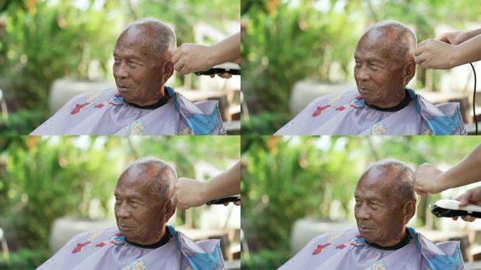 在检疫冠状病毒期间，亚洲妇女正在自家后院剪发和修剪老人的头发。