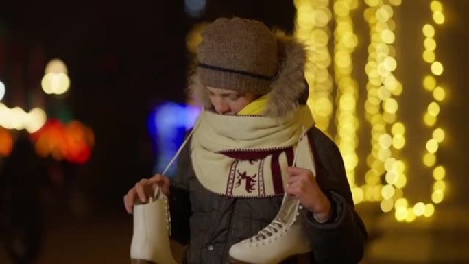 快乐的高加索男孩吹嘘新的溜冰鞋站在夜城新年，背景是金色的圣诞灯。兴奋的孩子吹牛节日礼物的肖像