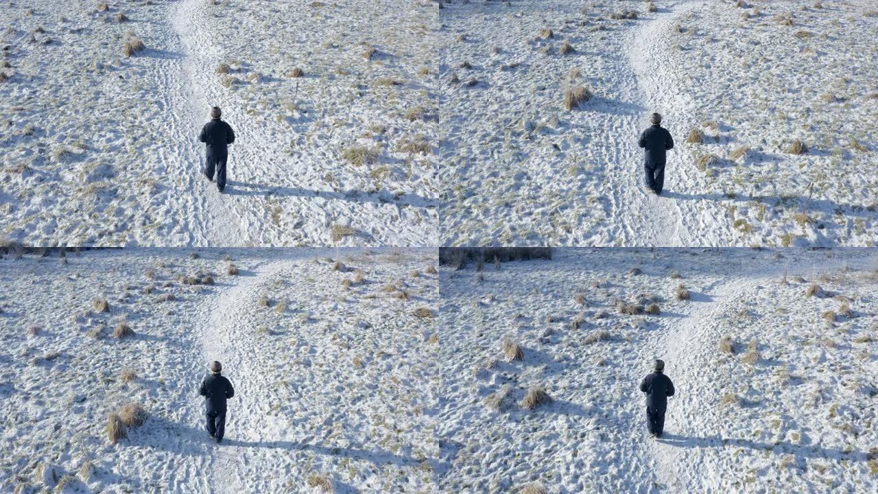 一名高级男子的无人驾驶飞机在苏格兰西南部积雪覆盖的人行道上独自行走时看到的后视图