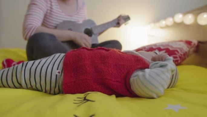 在家休闲。母亲带着一个小孩在卧室里弹吉他，同时照顾她刚出生的婴儿。新型冠状病毒肺炎大流行期间呆在家里