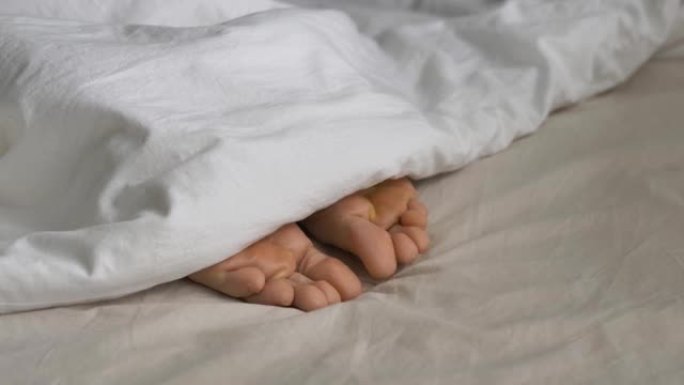 被毯子覆盖的昏昏欲睡的人在床上扭动脚趾