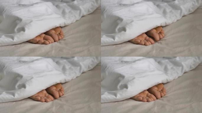 被毯子覆盖的昏昏欲睡的人在床上扭动脚趾