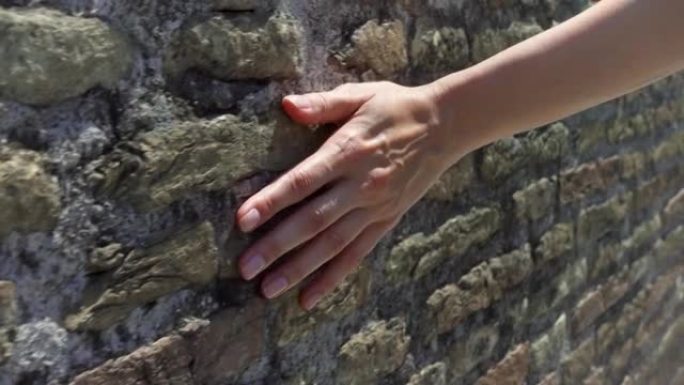 女人以慢动作将手滑到旧的红砖墙上。女性手触摸石头的粗糙表面