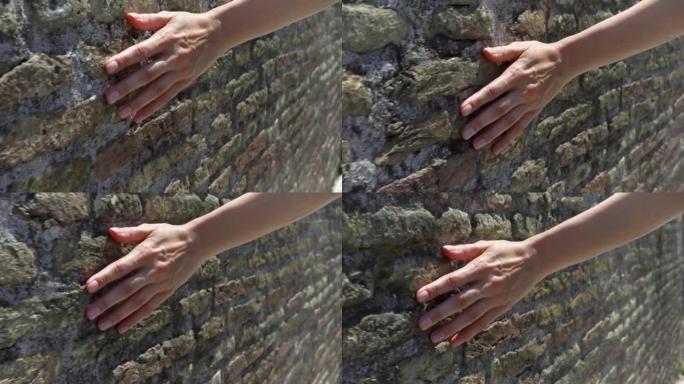 女人以慢动作将手滑到旧的红砖墙上。女性手触摸石头的粗糙表面