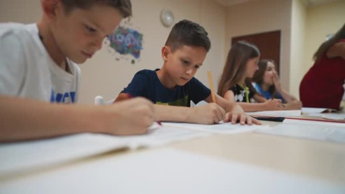 两个年轻的男生在小学教室里的笔记本上写字