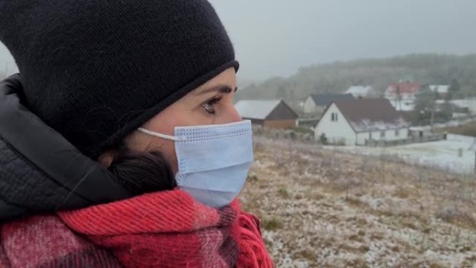 一名戴着医用口罩的40岁妇女的肖像站在小山上，背景是乡村房屋。冠状病毒新型冠状病毒肺炎大流行病毒。冠
