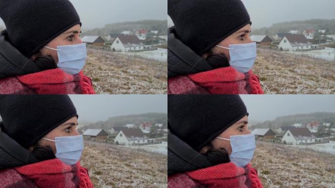 一名戴着医用口罩的40岁妇女的肖像站在小山上，背景是乡村房屋。冠状病毒新型冠状病毒肺炎大流行病毒。冠