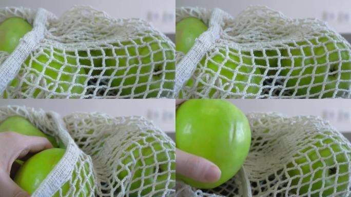 大圆青苹果堆放在白色的菜网中。一个苹果用手从网中取出。健康饮食。水果