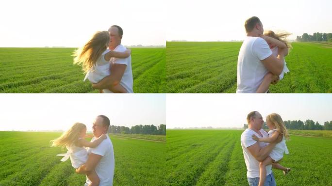 父亲和快乐的童女女儿在绿野日落。父亲和小女儿一起玩。他拥抱她。美丽，自然，健康，爱情，童年，幸福家庭
