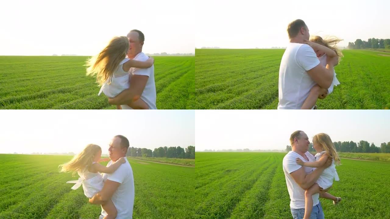 父亲和快乐的童女女儿在绿野日落。父亲和小女儿一起玩。他拥抱她。美丽，自然，健康，爱情，童年，幸福家庭