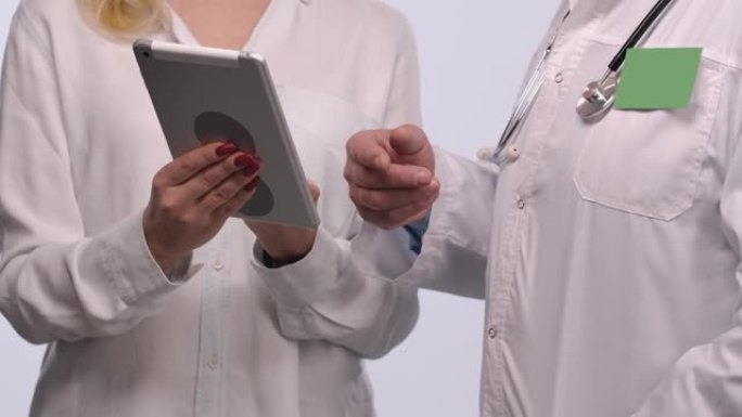 在医院的女性患者咨询期间，家庭医生会在平板电脑上交谈并显示信息。男士医生穿着白色医疗礼服，徽章绿色屏
