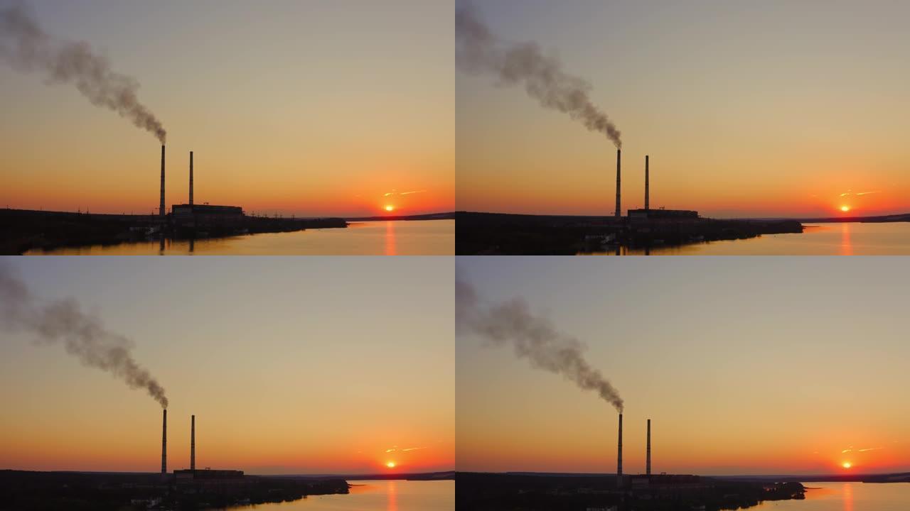 在橙色的天空中抽烟。日落时自然中的工业。从工厂释放到空气中的有害烟雾。