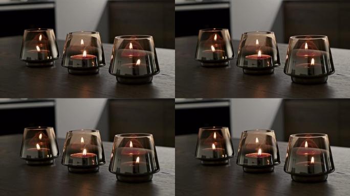 在家里的木桌上放着一排装有火焰蜡烛的玻璃杯