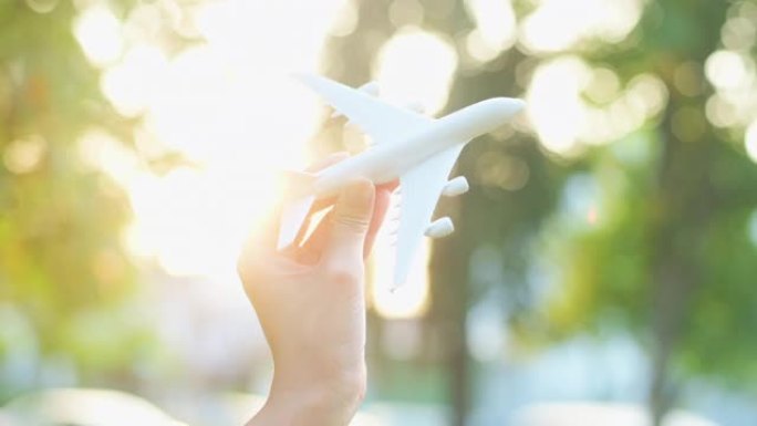 女人的手是在日落时手持飞机模型，假日旅行，商务节约运输理念。