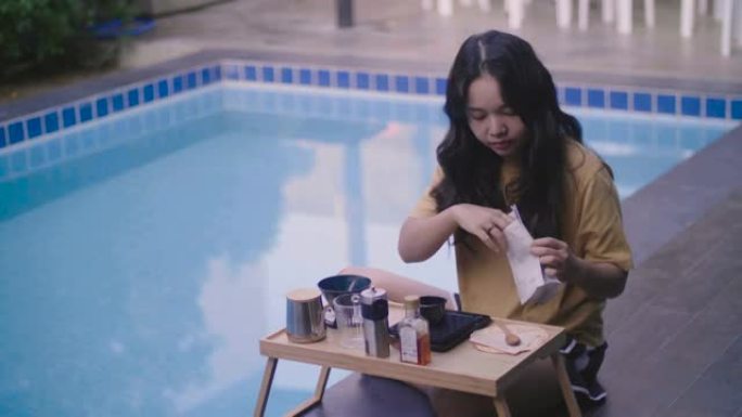 准备在游泳池旁的木桌旁煮咖啡的年轻女子。
