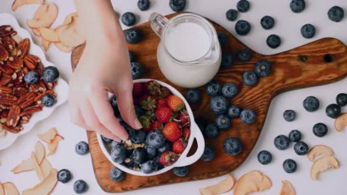 女人用手将浆果放入带有格兰诺拉麦片，蓝莓和草莓的陶瓷碗中