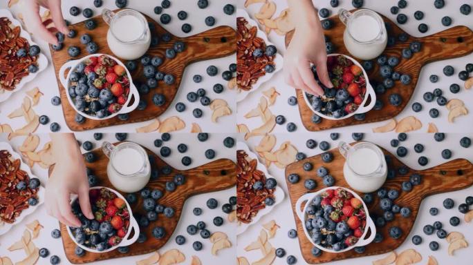 女人用手将浆果放入带有格兰诺拉麦片，蓝莓和草莓的陶瓷碗中