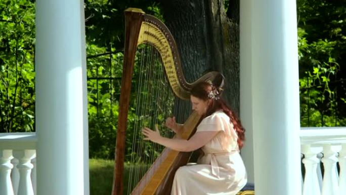 一个红头发的女人在公园的凉亭里演奏竖琴。慢动作