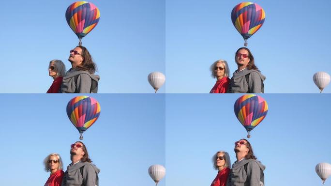 中年夫妇看着气球飞翔。男人和女人一起用彩色气球看着蓝天