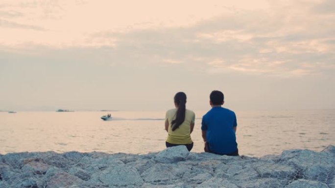 年轻夫妇跑步后休息，坐在海边看着美丽的日落。健康生活方式的概念。