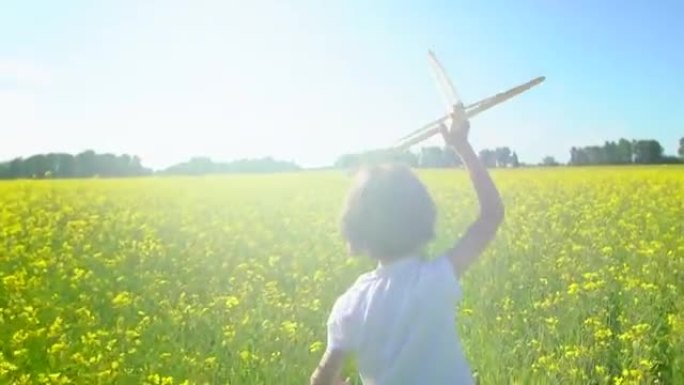 快乐的小男孩在黄花田里用玩具飞机奔跑。孩子在户外夏天玩飞机。小飞行员梦想着飞行，和幸福的家人一起度假