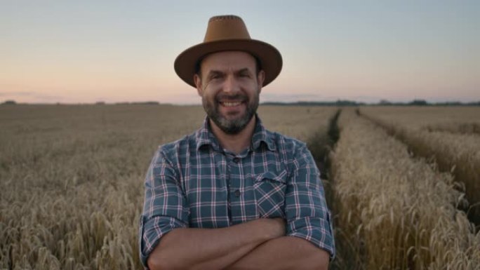 肖像高加索农民男子穿着帽子的格子衬衫看着相机。农田日落景观农业。肖像农民留着帽子的男人站在麦田里。农