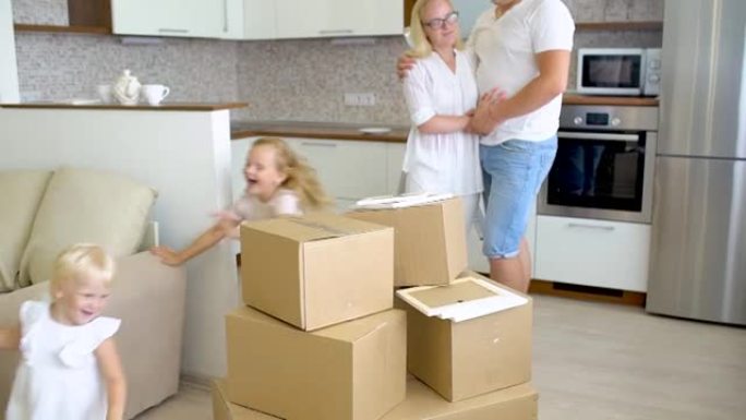 年轻幸福的家庭搬到新公寓。两个小女孩和父母在背景纸板箱里跑进新家，幸福的夫妇和孩子们搬进了新房子。搬