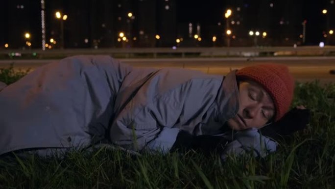 无家可归的人在高速公路附近夜城背景下的草坪上睡着了