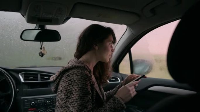 年轻女子在外面下雨时在车内打电话。