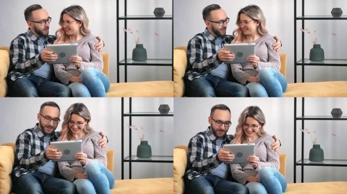 开朗的夫妇微笑拥抱一起使用平板电脑在家放松。4k龙红相机