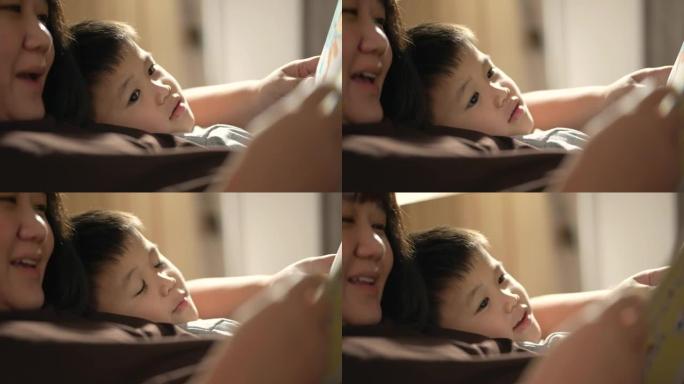 亚洲孩子和母亲在卧室里读睡前故事。家庭时间的概念