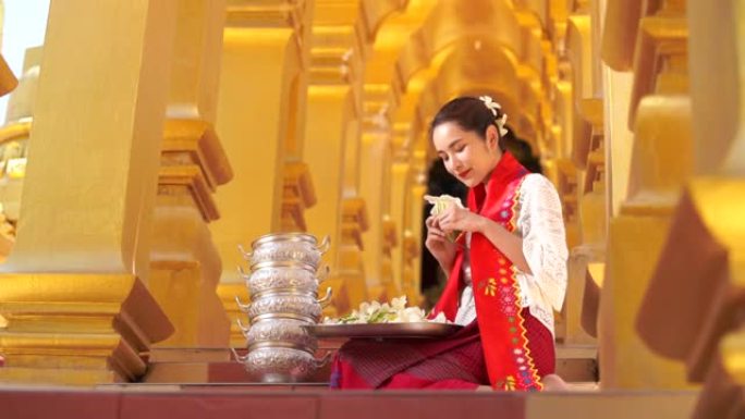 缅甸妇女手拿鲜花。穿着缅甸传统服装的东南亚年轻女孩参观Buddihist寺庙