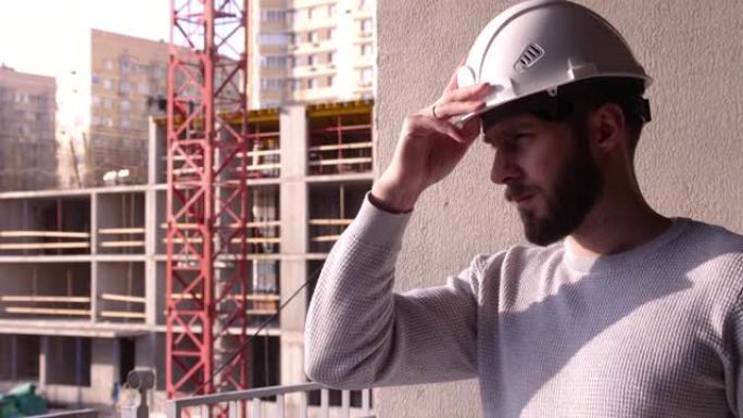 年轻的土木工程师，在建筑工地戴着白色安全帽，留着胡须。专业男性建筑工人戴上白色建筑头盔。