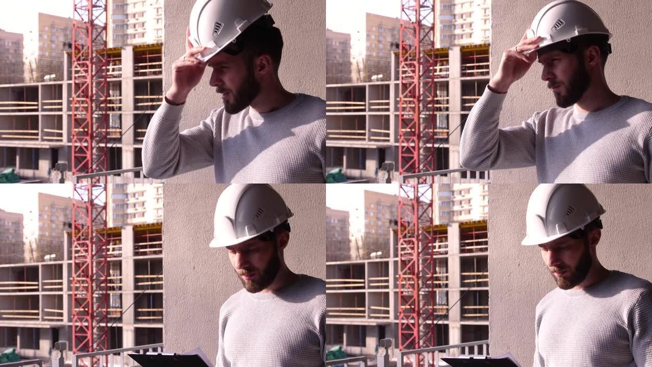 年轻的土木工程师，在建筑工地戴着白色安全帽，留着胡须。专业男性建筑工人戴上白色建筑头盔。