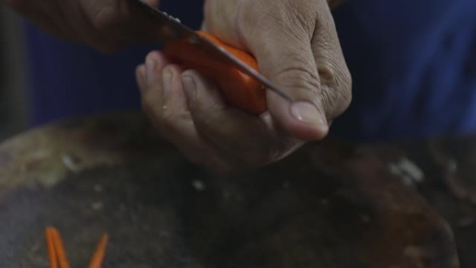 用小刀在木砧板上手切胡萝卜。