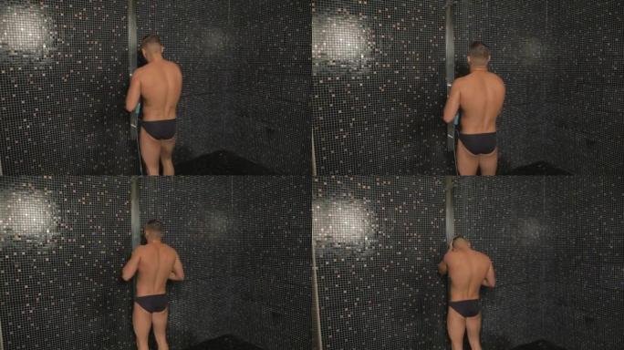 游泳裤中的运动员在锻炼后进入黑色设计淋浴，打开水并开始清洗