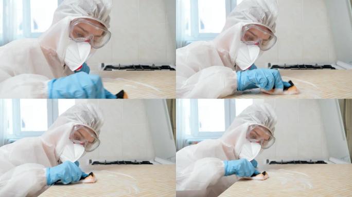 家庭主妇戴着医用手套，口罩nad防护服用化学洗涤剂和海绵清洁和清洗厨房桌面
