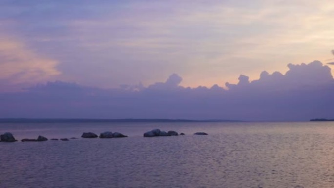 平静的海面上的紫色日落，明亮的阳光照耀着傍晚的云层