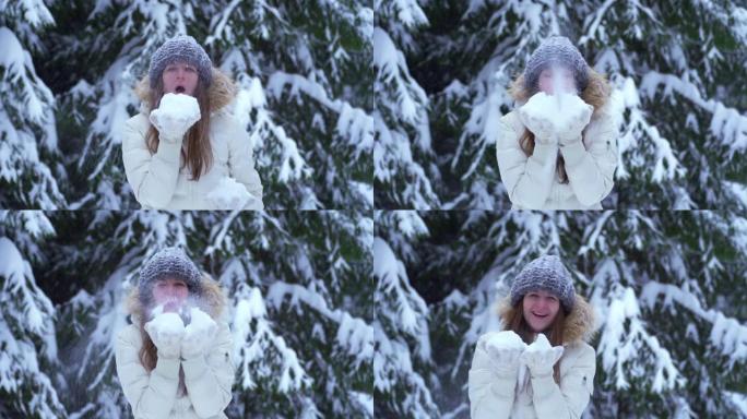 女人从手掌吹雪。把雪吹进相机里。冬天，在树木间的白雪皑皑的森林里，雪球在一个美丽的高加索女人手中。飘