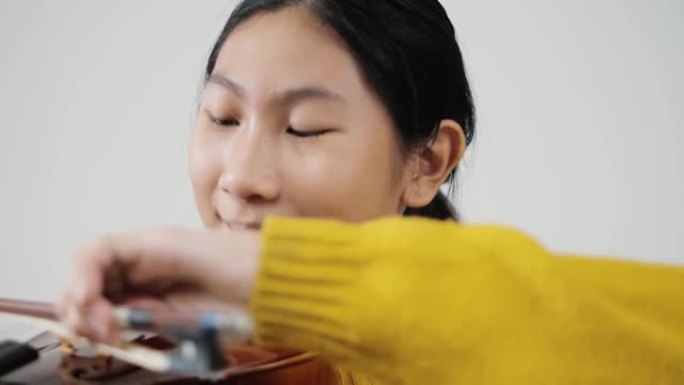 穿着黄色毛衣的亚洲女学生学习小提琴与灰色背景，生活方式概念。