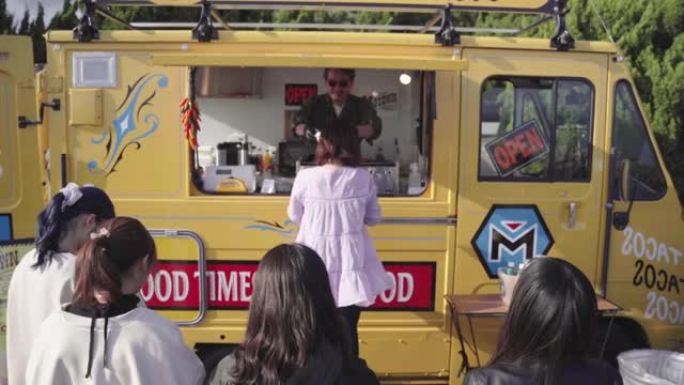 一名年轻女子从食品卡车上买午餐的中等镜头，她身后有一条线