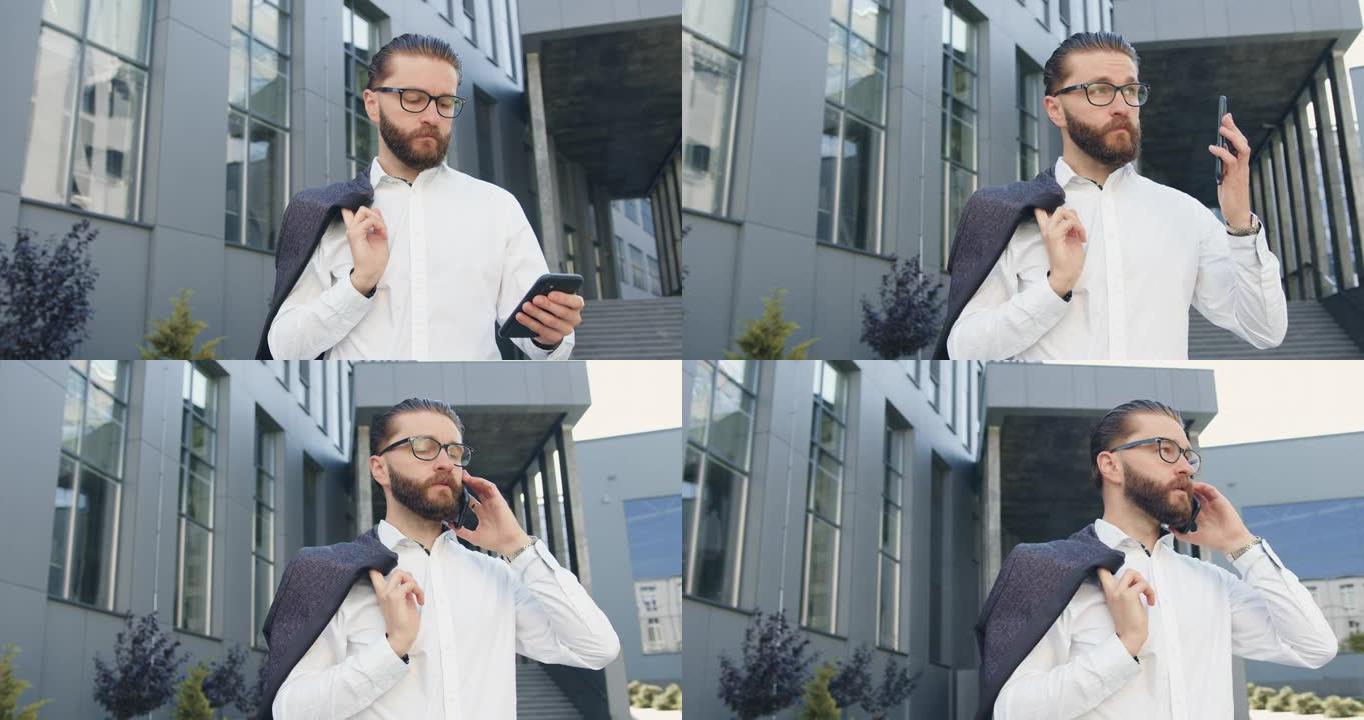 有吸引力的严重内敛成功的年轻胡须企业工人站在现代城市建筑的背景下，与商业伙伴进行电话交谈