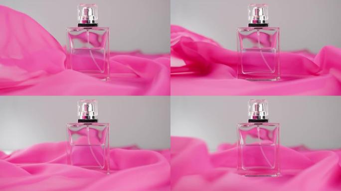 白色桌子上放着带有青色香水或精油的扁平瓶子。粉红色的织物四处飘动，瓶子周围的空气中飘扬。香气和气味的