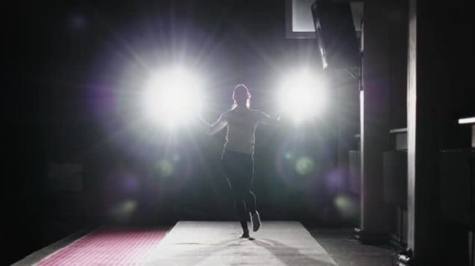全身苗条的女性在黑暗的健身房里对着明亮的聚光灯行走和跳舞