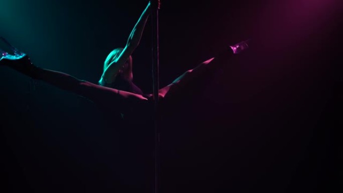 性感的金发女郎爬上杆子，使麻线和性下降。钢管舞。在黑暗的工作室拍摄，有烟雾和霓虹灯。明亮的蓝色和紫色